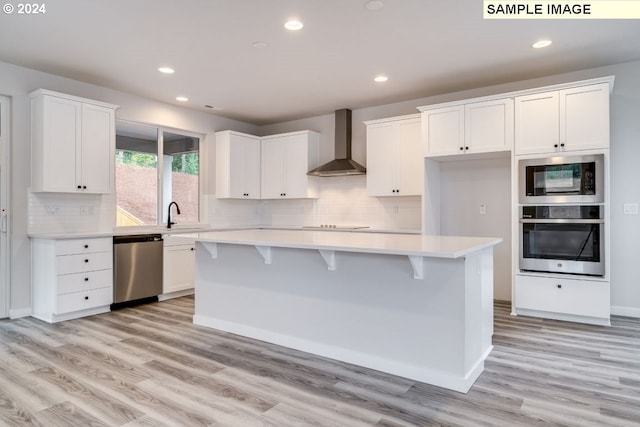 kitchen with wall chimney range hood, stainless steel appliances, white cabinets, and a kitchen island