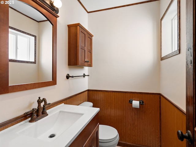 bathroom with toilet, ornamental molding, wood walls, and vanity