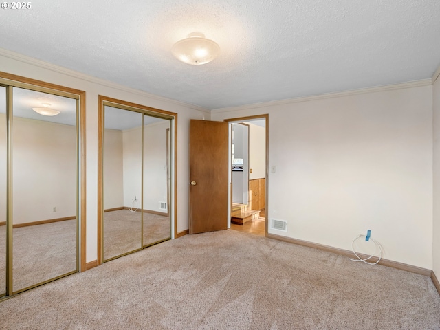 unfurnished bedroom with a textured ceiling, crown molding, light carpet, and multiple closets