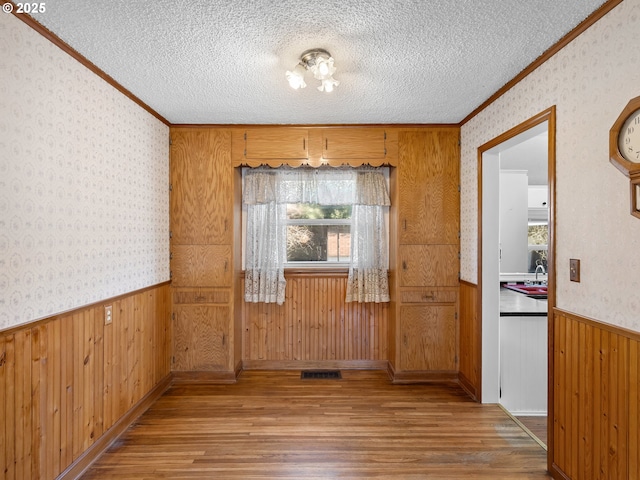 unfurnished dining area with wood-type flooring, sink, ornamental molding, and a textured ceiling