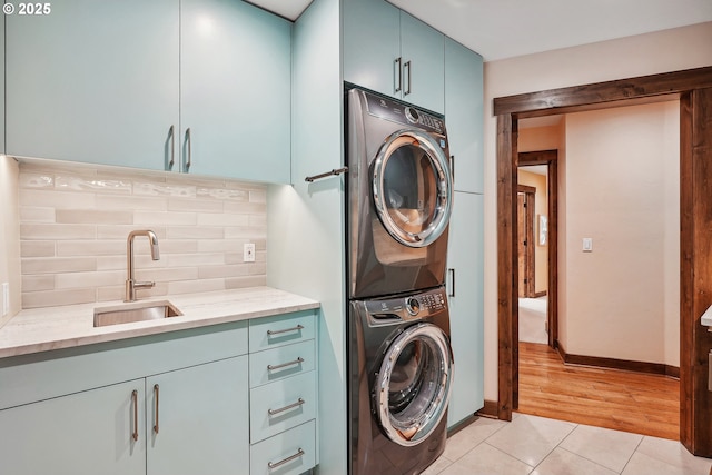 washroom featuring baseboards, stacked washer and dryer, light tile patterned floors, cabinet space, and a sink