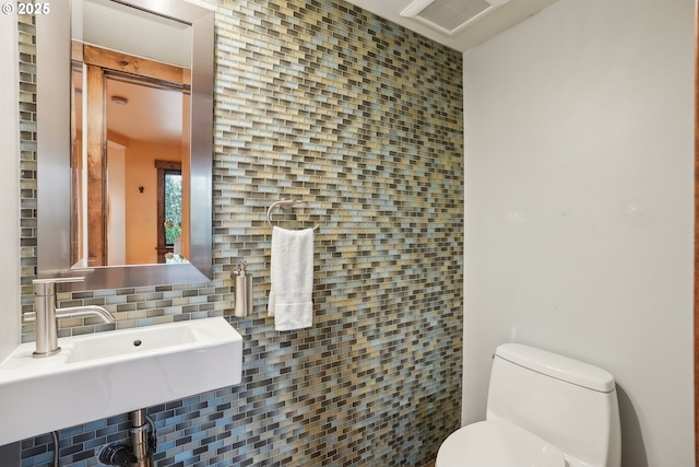 half bath with tasteful backsplash, visible vents, toilet, and a sink