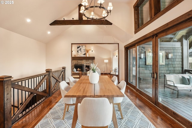 dining area featuring dark wood-style flooring, a stone fireplace, a chandelier, french doors, and beam ceiling