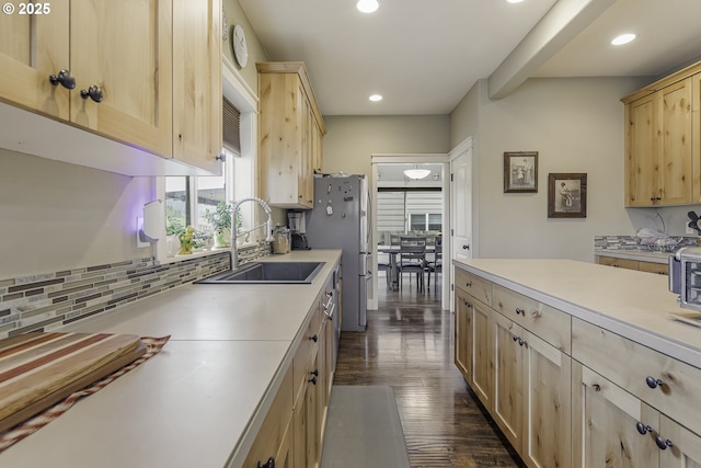 kitchen with light countertops, freestanding refrigerator, light brown cabinets, and a sink