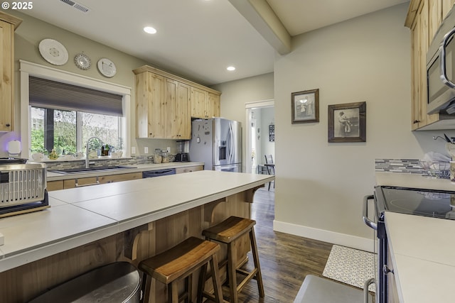 kitchen featuring a breakfast bar area, dark wood-style flooring, stainless steel appliances, light brown cabinetry, and a sink