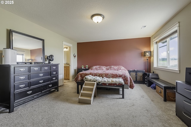 bedroom featuring carpet floors, visible vents, a textured ceiling, and ensuite bathroom