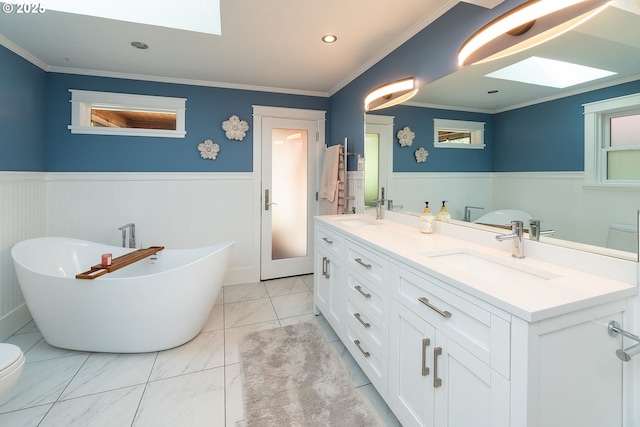 full bathroom featuring a skylight, a wainscoted wall, toilet, marble finish floors, and a soaking tub
