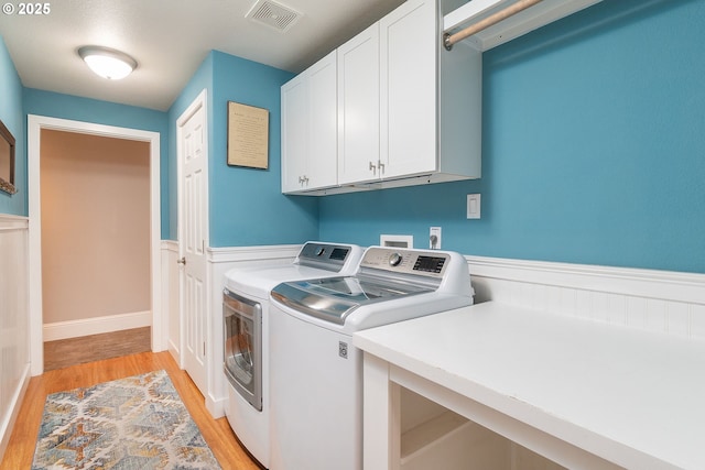 washroom with cabinet space, washing machine and dryer, light wood finished floors, and wainscoting