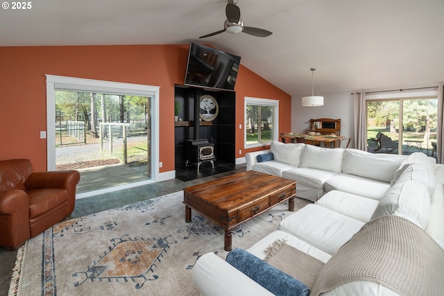 living room with a wood stove, lofted ceiling, ceiling fan, healthy amount of natural light, and baseboards