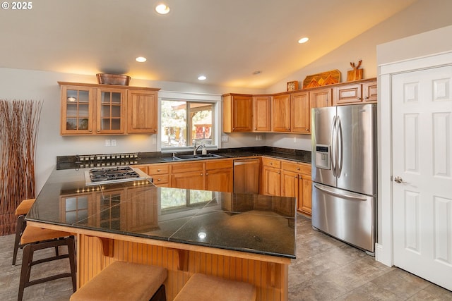 kitchen featuring appliances with stainless steel finishes, a sink, a kitchen breakfast bar, glass insert cabinets, and brown cabinets