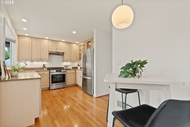 kitchen with stainless steel appliances, under cabinet range hood, a sink, glass insert cabinets, and light wood finished floors