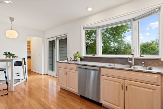 kitchen with dishwasher, a sink, light brown cabinets, light wood finished floors, and dark countertops