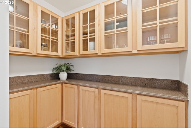 kitchen featuring light brown cabinetry, glass insert cabinets, and dark countertops