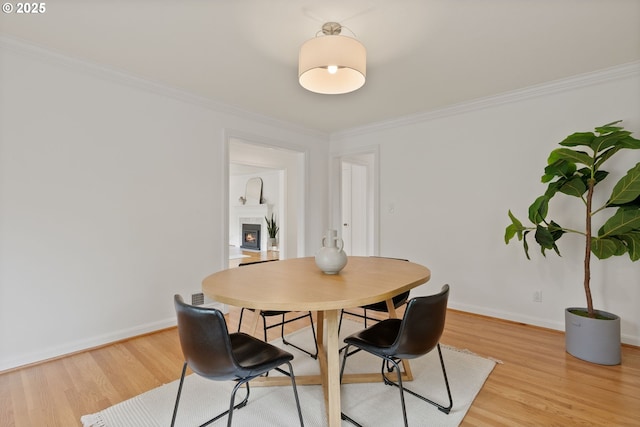 dining space with light wood-style floors, ornamental molding, a lit fireplace, and baseboards