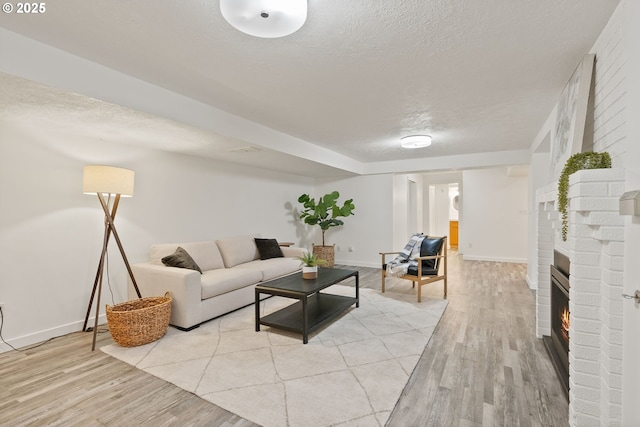 living room featuring a textured ceiling, light wood finished floors, baseboards, and a brick fireplace