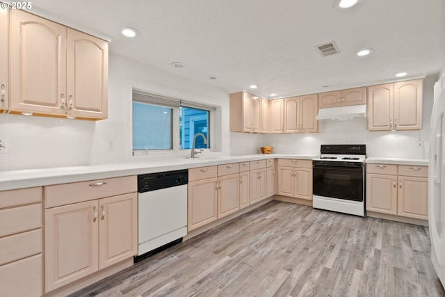 kitchen with white appliances, under cabinet range hood, a sink, light wood-style flooring, and light countertops