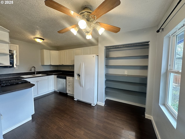 kitchen featuring dark countertops, stainless steel dishwasher, a sink, white fridge with ice dispenser, and a textured ceiling