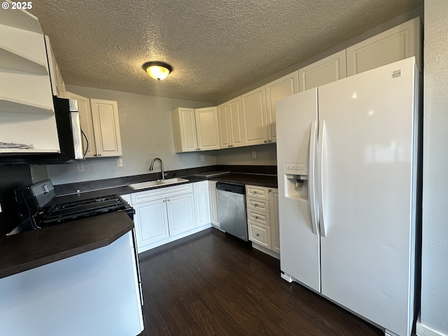 kitchen with dark wood finished floors, stainless steel appliances, dark countertops, a sink, and white cabinetry
