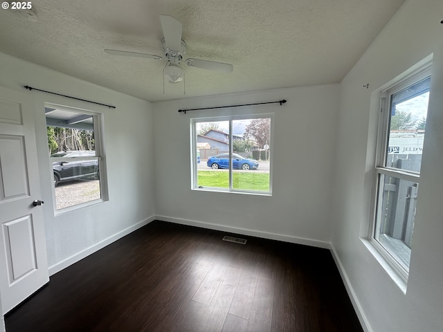 unfurnished room with baseboards, visible vents, a textured ceiling, and dark wood finished floors