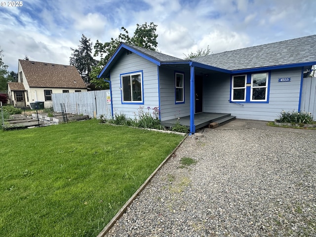 view of front facade featuring fence, a shingled roof, and a front lawn