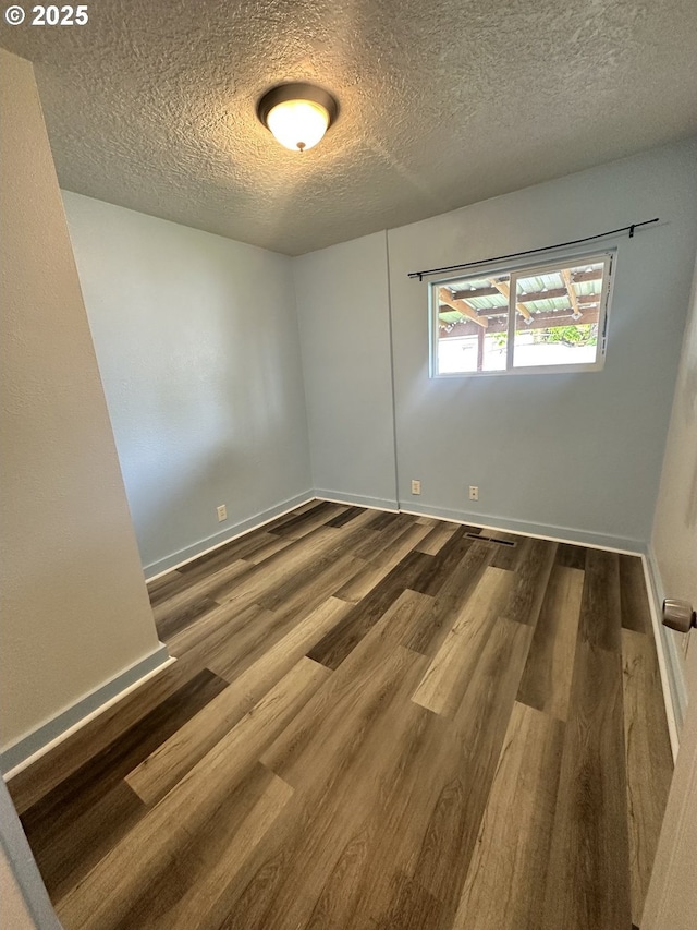 spare room with baseboards, wood finished floors, and a textured ceiling