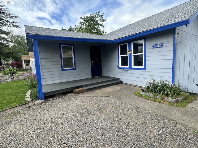 view of exterior entry featuring a shingled roof and covered porch