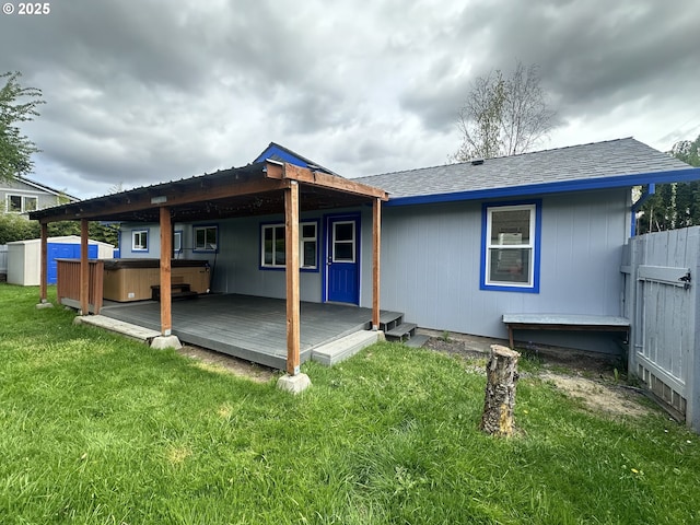back of property featuring a wooden deck, fence, a hot tub, and a yard