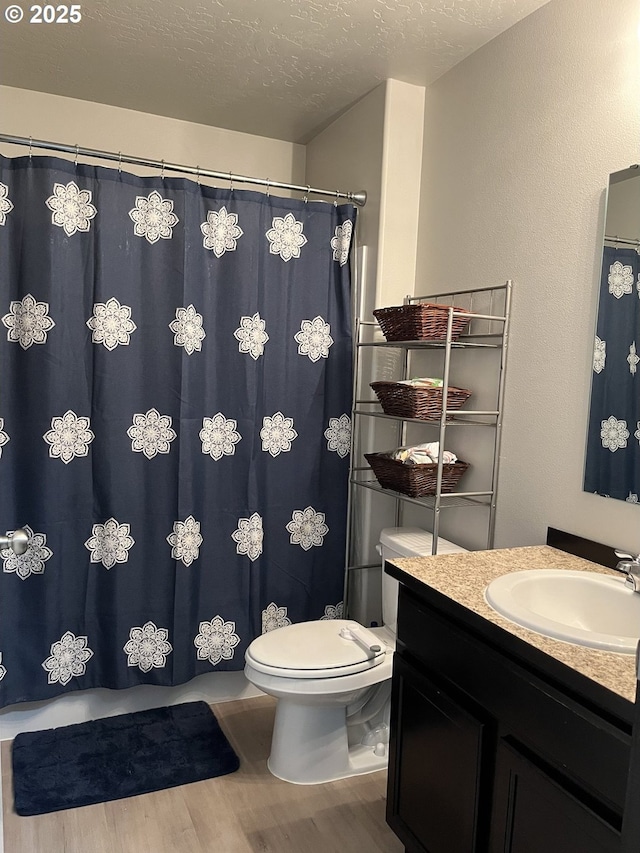 bathroom with a textured ceiling, curtained shower, toilet, wood finished floors, and vanity