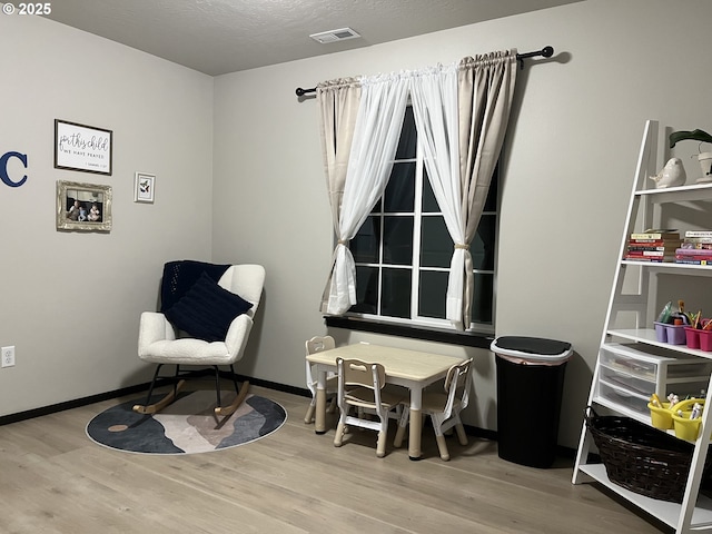 living area with visible vents, a textured ceiling, baseboards, and wood finished floors