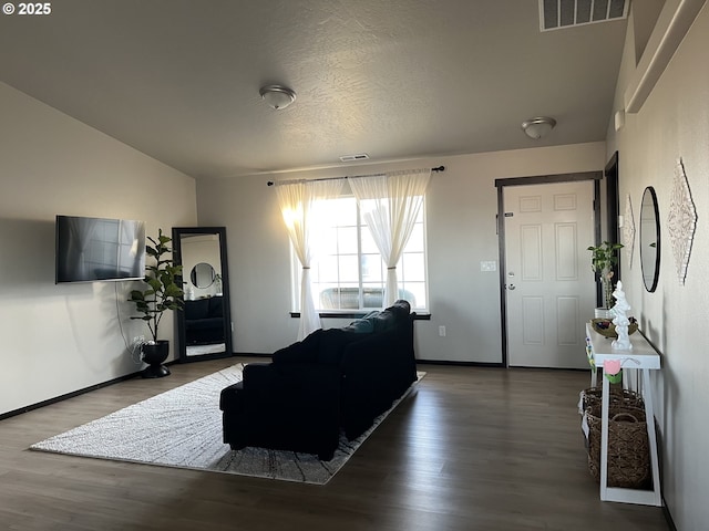 living room with visible vents, a textured ceiling, baseboards, and wood finished floors