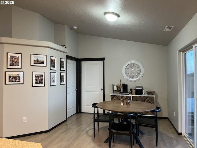 dining area with a textured ceiling, light wood-style flooring, visible vents, and baseboards