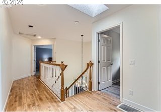 hall with wood finished floors, an upstairs landing, and baseboards