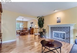 living room featuring a tiled fireplace, light wood-style flooring, arched walkways, and baseboards