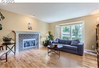 living room featuring a tiled fireplace, light wood-style flooring, and baseboards