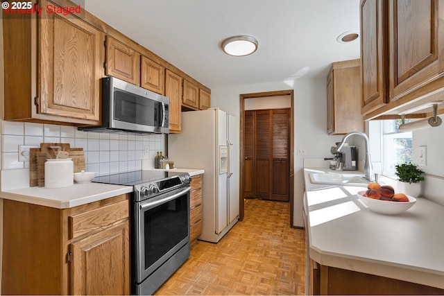 10915 SW Meadowbrook Dr Unit 22, Portland, OR 97224 - kitchen featuring stainless steel appliances, tasteful backsplash, light countertops, and brown cabinets