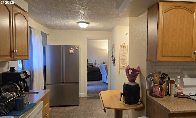 kitchen with a textured ceiling, stainless steel refrigerator, and backsplash