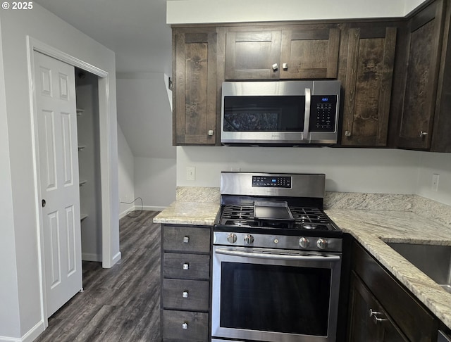 kitchen featuring appliances with stainless steel finishes, dark wood-type flooring, light stone counters, dark brown cabinetry, and sink