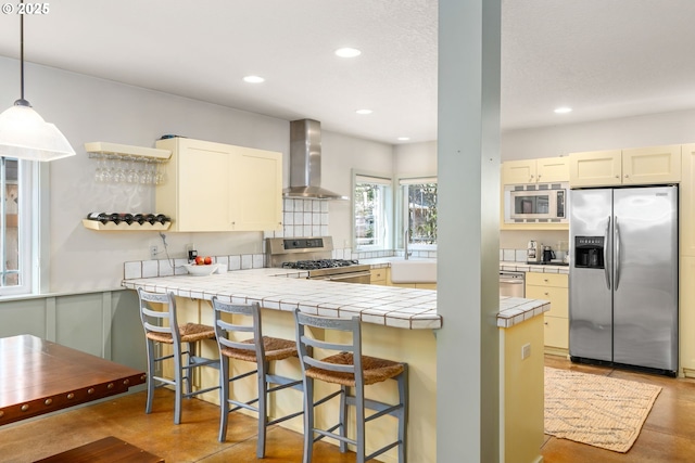 kitchen with tile countertops, wall chimney exhaust hood, recessed lighting, and appliances with stainless steel finishes