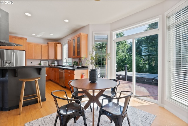 kitchen with appliances with stainless steel finishes, dark countertops, extractor fan, glass insert cabinets, and light wood finished floors