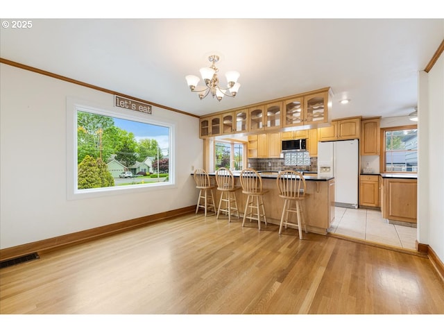 kitchen featuring glass insert cabinets, white refrigerator with ice dispenser, stainless steel microwave, light wood finished floors, and a notable chandelier
