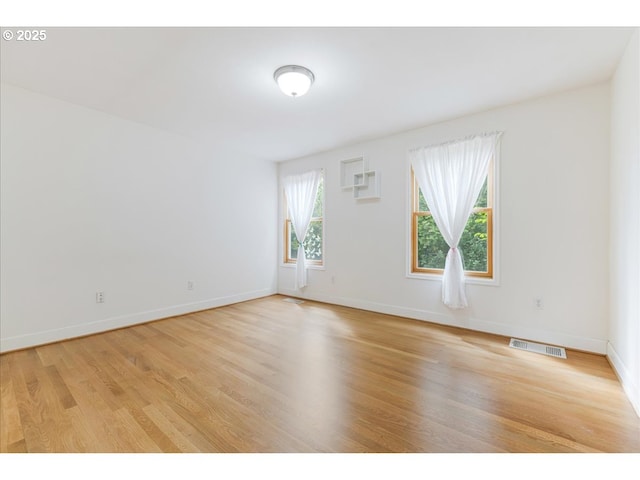 empty room featuring baseboards, light wood-type flooring, and visible vents