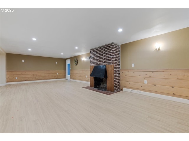 unfurnished living room with wooden walls, wainscoting, a fireplace, recessed lighting, and light wood-type flooring