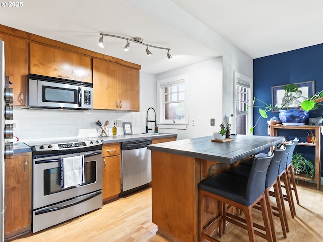 kitchen with appliances with stainless steel finishes, tasteful backsplash, light hardwood / wood-style floors, sink, and tile countertops