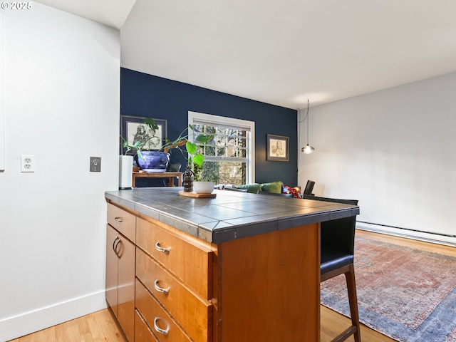 kitchen with light hardwood / wood-style floors, a baseboard radiator, kitchen peninsula, and tile countertops