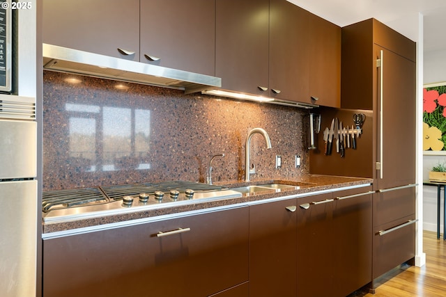 kitchen with stainless steel gas stovetop, sink, decorative backsplash, light wood-type flooring, and dark brown cabinets