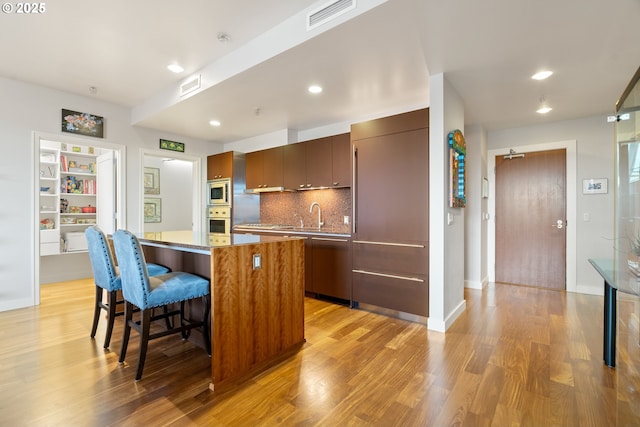 kitchen featuring backsplash, appliances with stainless steel finishes, a breakfast bar, a kitchen island, and light wood-type flooring