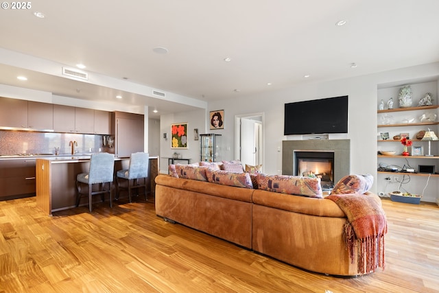 living room with built in features, light hardwood / wood-style flooring, a tile fireplace, and sink