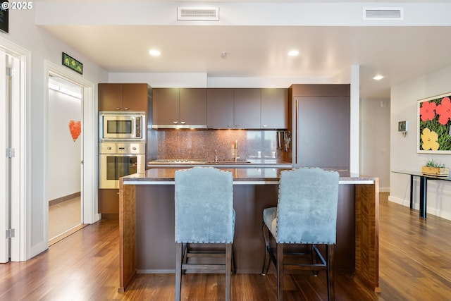 kitchen featuring a kitchen breakfast bar, dark hardwood / wood-style flooring, backsplash, a kitchen island, and appliances with stainless steel finishes