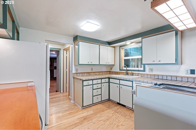 kitchen featuring tile countertops, white cabinetry, a sink, freestanding refrigerator, and light wood-style flooring