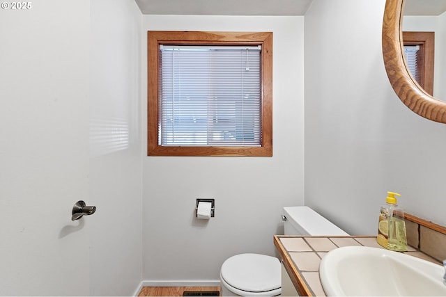 half bath with baseboards, vanity, toilet, and wood finished floors
